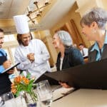 Restaurant chef and waiter helping customers with menu food questions.