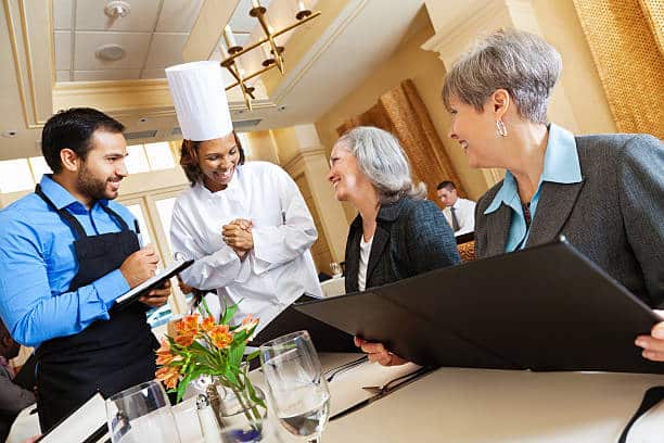 Restaurant chef and waiter helping customers with menu food questions.